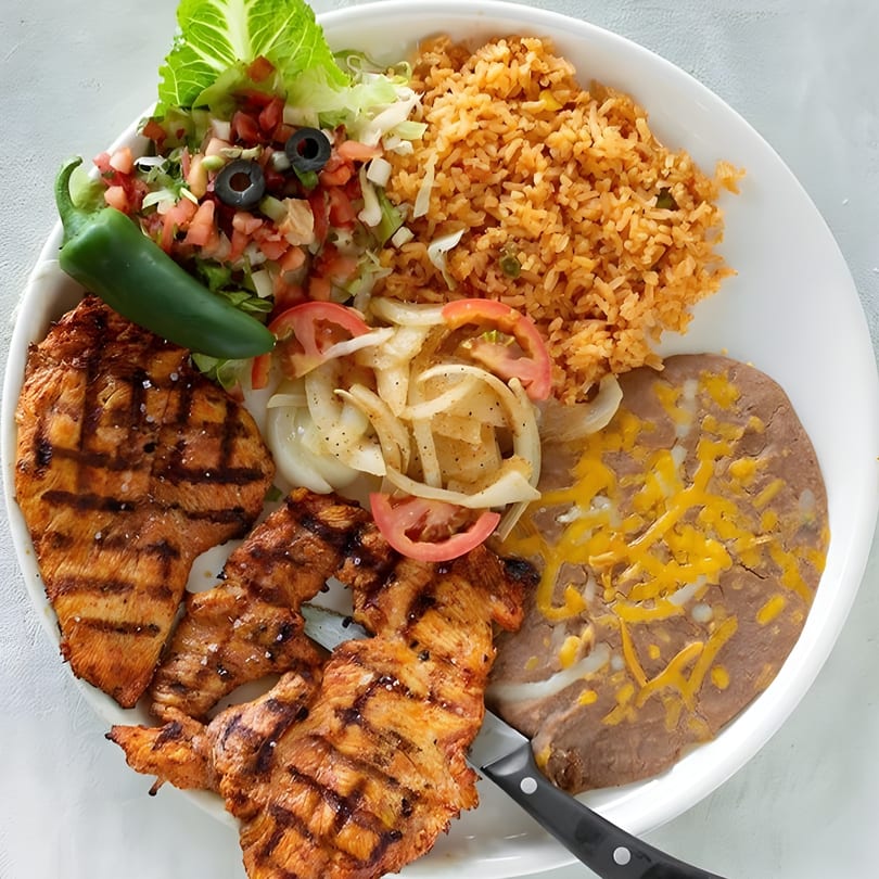 Grilled chicken with rice, refried beans, salad, and a jalapeño on a white plate.