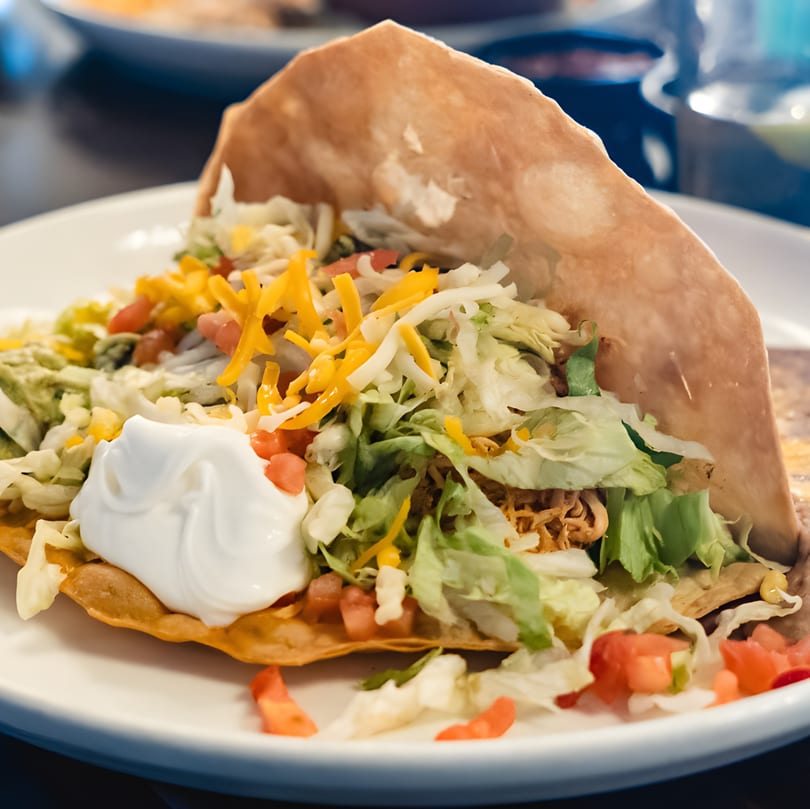 A crispy taco from Luna Mexican Cuisine, filled with meat, lettuce, cheese, tomatoes, and sour cream.
