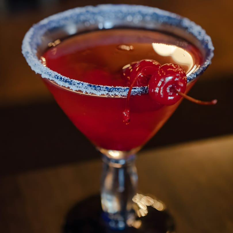A vibrant red cocktail with two cherries and a sugar-rimmed glass at Luna Mexican Cuisine.