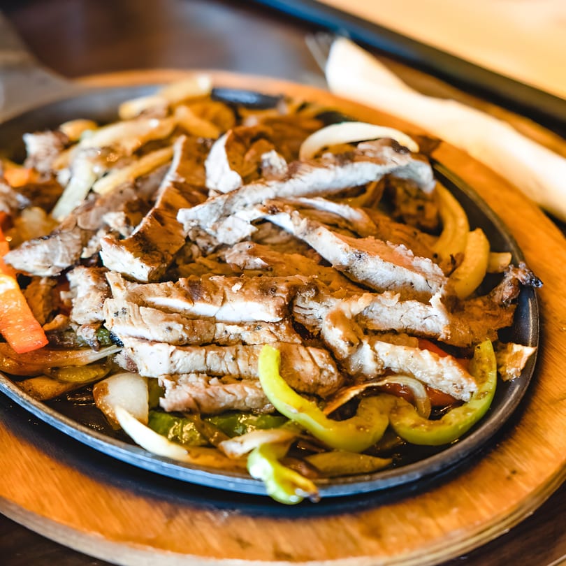 Sizzling chicken fajitas with grilled onions and bell peppers on a cast iron skillet.