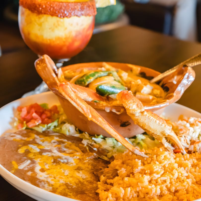 Mexican seafood dish with crab legs, rice, refried beans, and a chamoy-rimmed drink.
